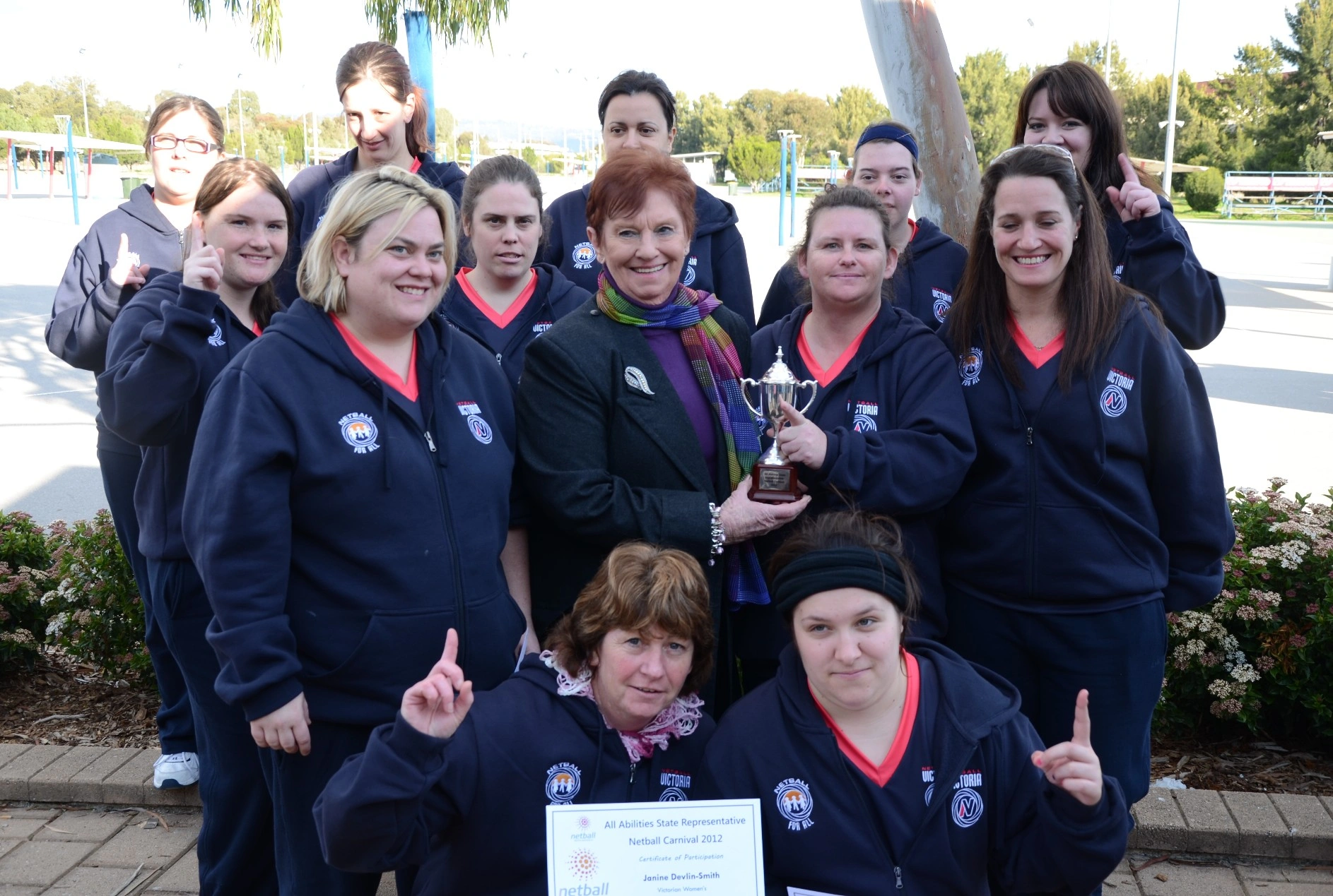 Marie Little holds a trophy and stands at the centre of the Victorian Netball team from the All Abilities State Representative Netball Carnival in 20212. 